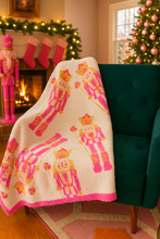 Load image into Gallery viewer, Decorative blanket with nutcracker design draped over a green chair, Christmas tree and stockings in the background.