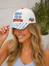 Load image into Gallery viewer, Woman wearing a white cap with 'Proud to be an American' text and an American flag design.