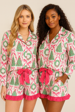 Load image into Gallery viewer, Two women wearing matching pink and green pajama sets with festive patterns on a beige background.
