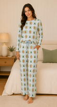 Load image into Gallery viewer, Woman wearing a patterned pajama set in a cozy living room.
