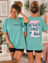 Load image into Gallery viewer, Two women modeling matching turquoise graphic T-shirts in a cozy indoor setting. The front view shows the text 'JESUS PAID IT ALL' in black with a pink heart outline, and the back view shows a large pink and blue graphic reading 'Jesus Paid It All'.
