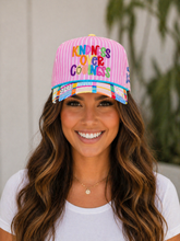 Load image into Gallery viewer, Woman wearing a pink cap with colorful text, smiling outdoors.
